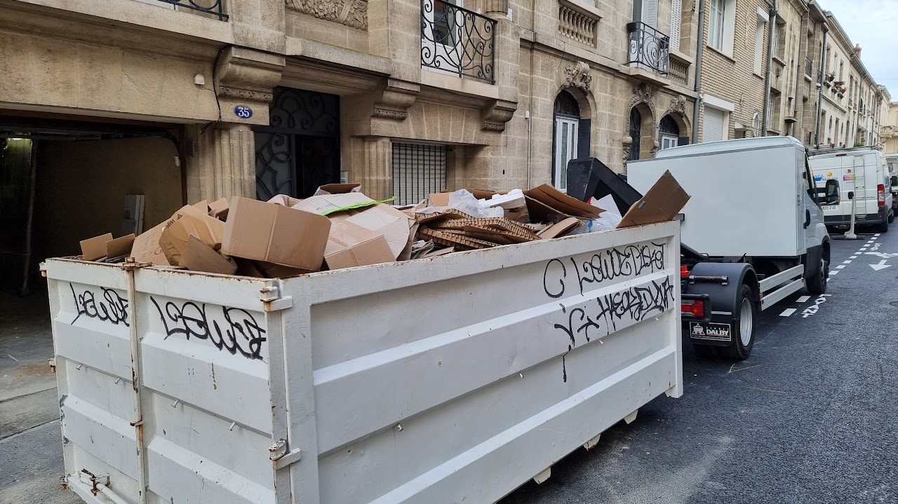 Benne remplie de cartons devant un immeuble du centre de Bordeaux